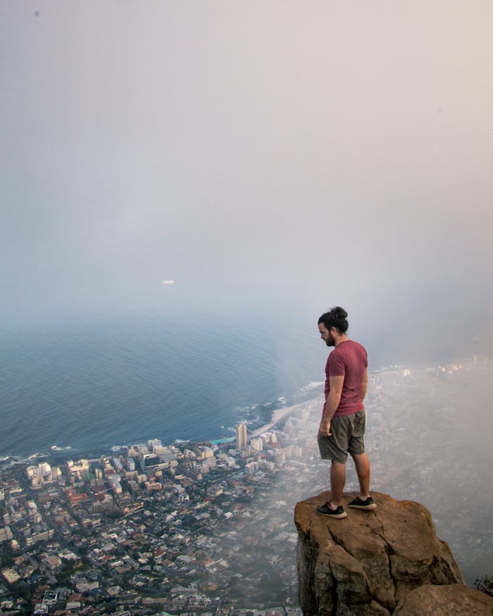 Man enjoys a foggy view of Cape Town from a cliff, exemplifying adventure and exploration.
